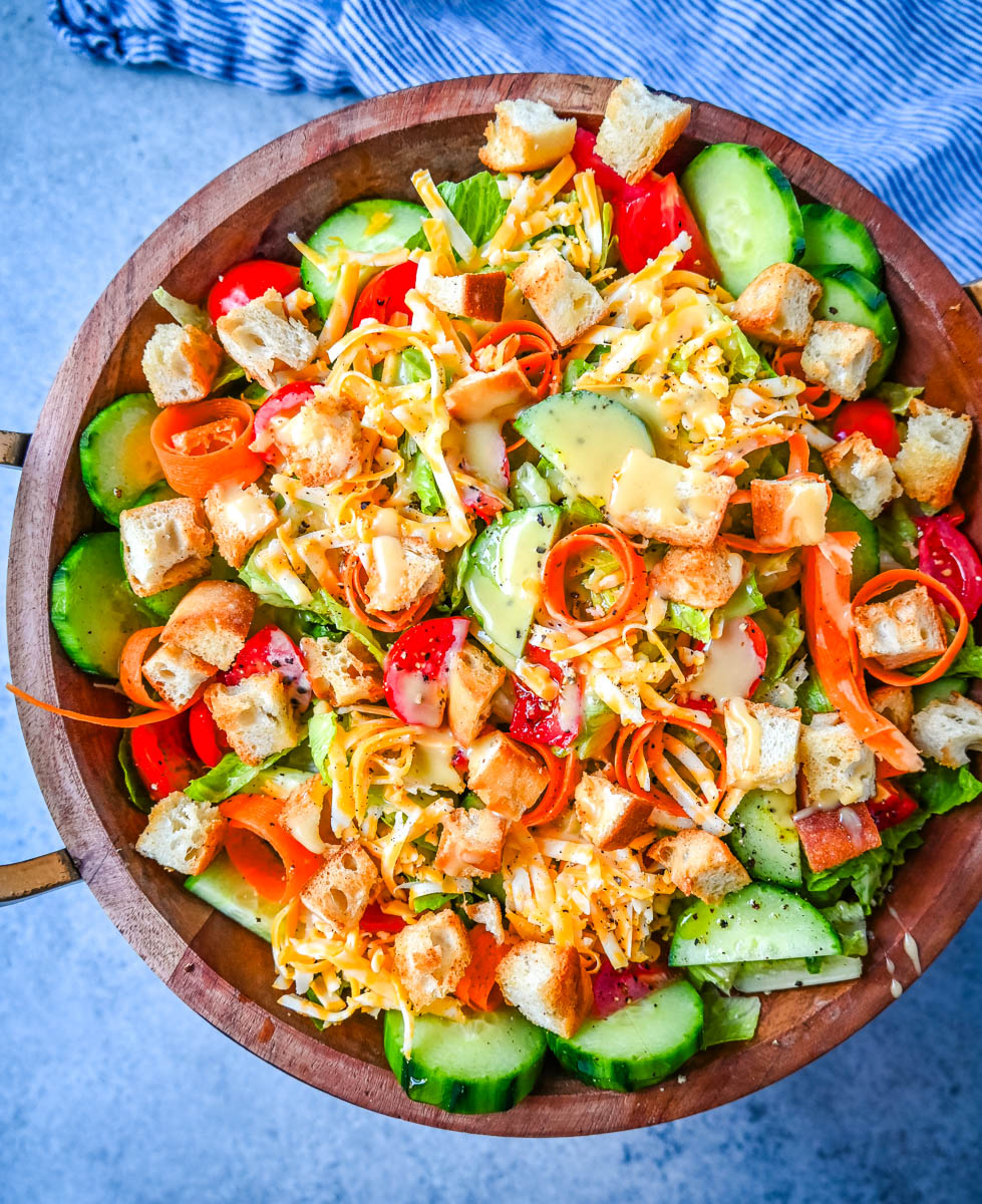 This fresh garden salad recipe is made with crisp lettuce, tomatoes, carrot ribbons, cucumbers, cheddar and mozzarella cheeses, homemade croutons, all tossed with a honey mustard or ranch dressing.