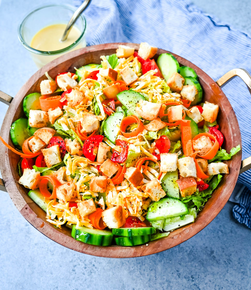 This fresh garden salad recipe is made with crisp lettuce, tomatoes, carrot ribbons, cucumbers, cheddar and mozzarella cheeses, homemade croutons, all tossed with a honey mustard or ranch dressing.