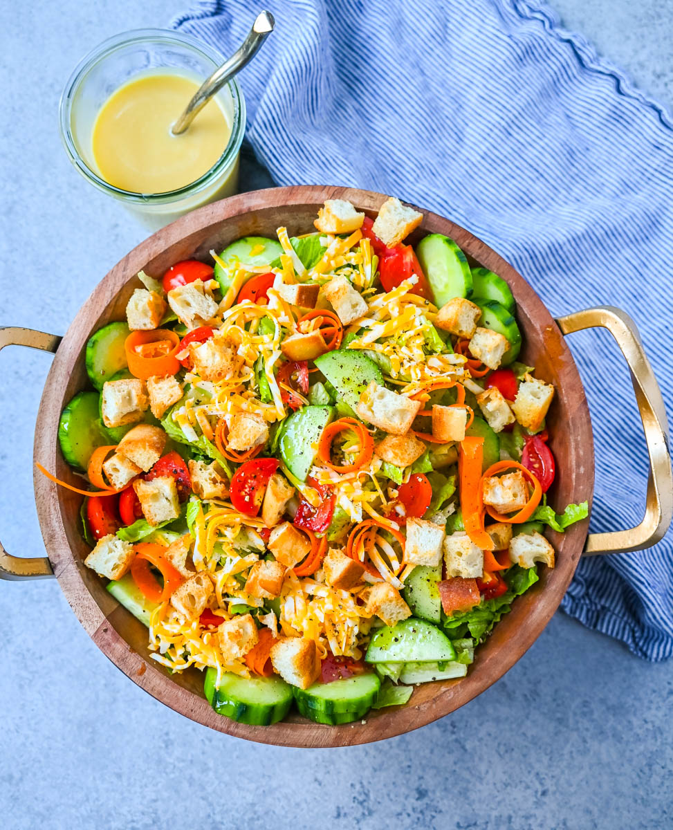 This fresh garden salad recipe is made with crisp lettuce, tomatoes, carrot ribbons, cucumbers, cheddar and mozzarella cheeses, homemade croutons, all tossed with a honey mustard or ranch dressing.