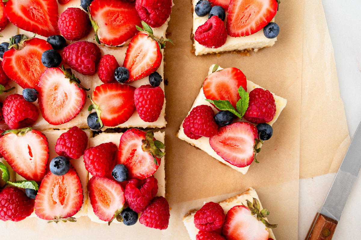 Creamy luscious cheesecake bars with a buttery graham cracker crust and topped with fresh berries is a crowd-pleasing popular dessert! They feature a creamy, tangy cheesecake filling atop a buttery graham cracker crust, baked to perfection in a bar form. Whether you're looking for a treat for a party, a family dessert, or simply craving cheesecake, these cheesecake bars are a hit.