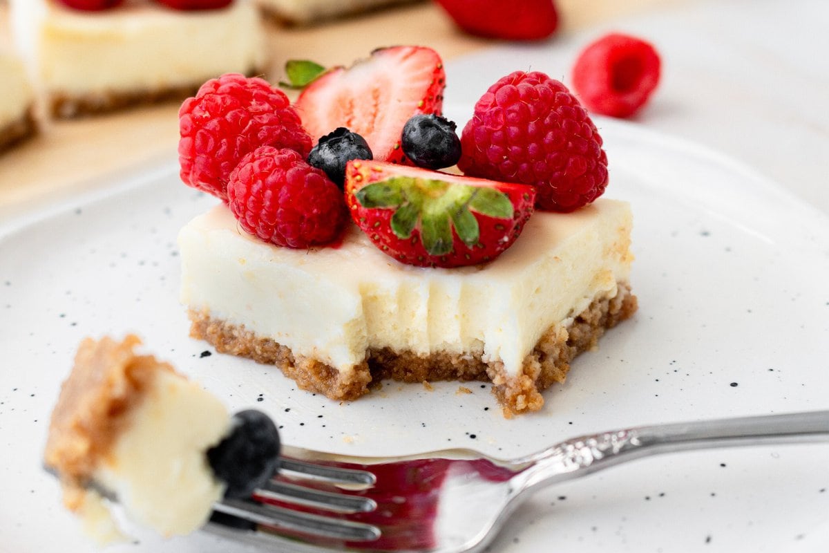 Creamy luscious cheesecake bars with a buttery graham cracker crust and topped with fresh berries is a crowd-pleasing popular dessert! They feature a creamy, tangy cheesecake filling atop a buttery graham cracker crust, baked to perfection in a bar form. Whether you're looking for a treat for a party, a family dessert, or simply craving cheesecake, these cheesecake bars are a hit.