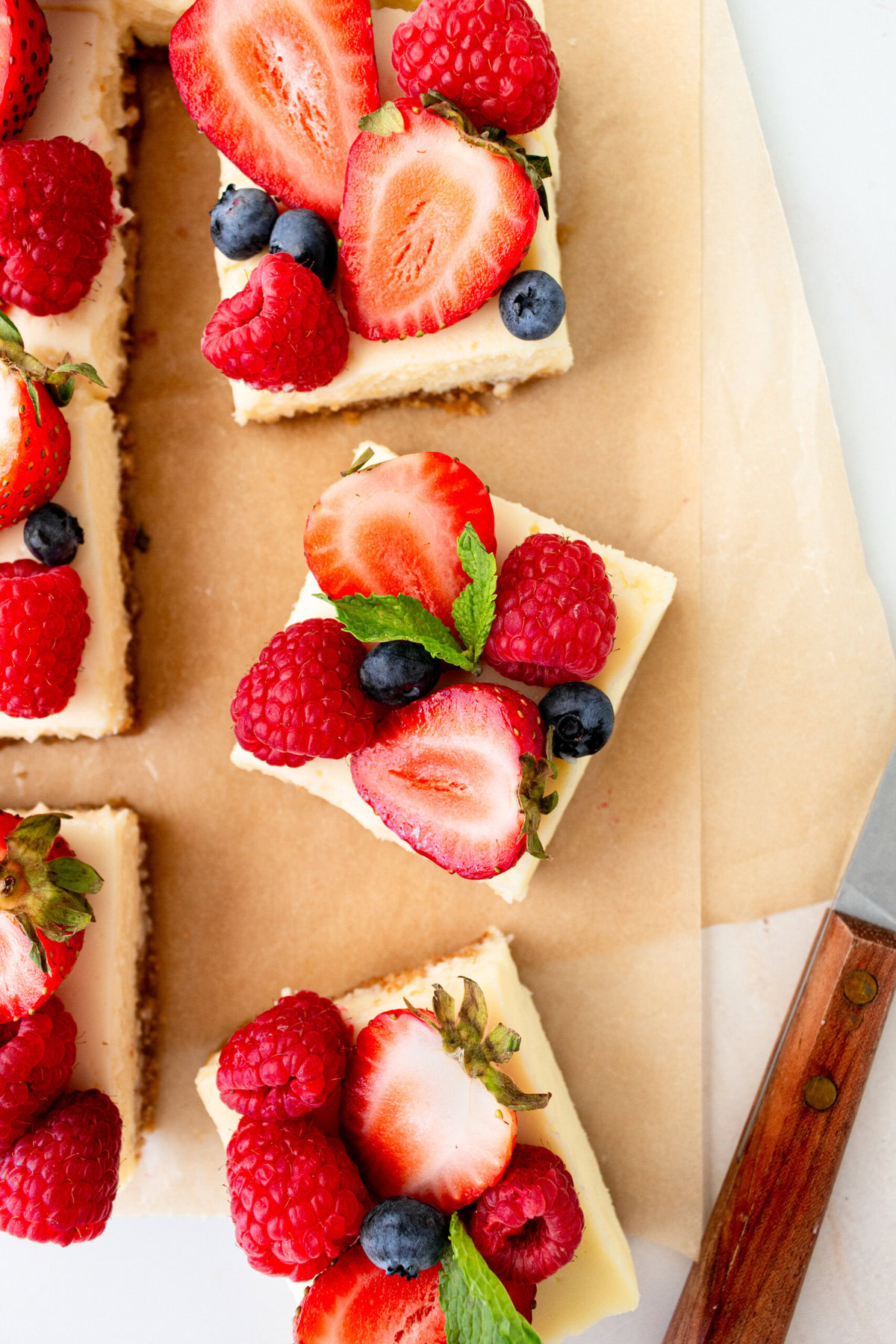 Creamy luscious cheesecake bars  cut into squares with a buttery graham cracker crust and topped with fresh berries is a crowd-pleasing popular dessert! They feature a creamy, tangy cheesecake filling atop a buttery graham cracker crust, baked to perfection in a bar form. Whether you're looking for a treat for a party, a family dessert, or simply craving cheesecake, these cheesecake bars are a hit.