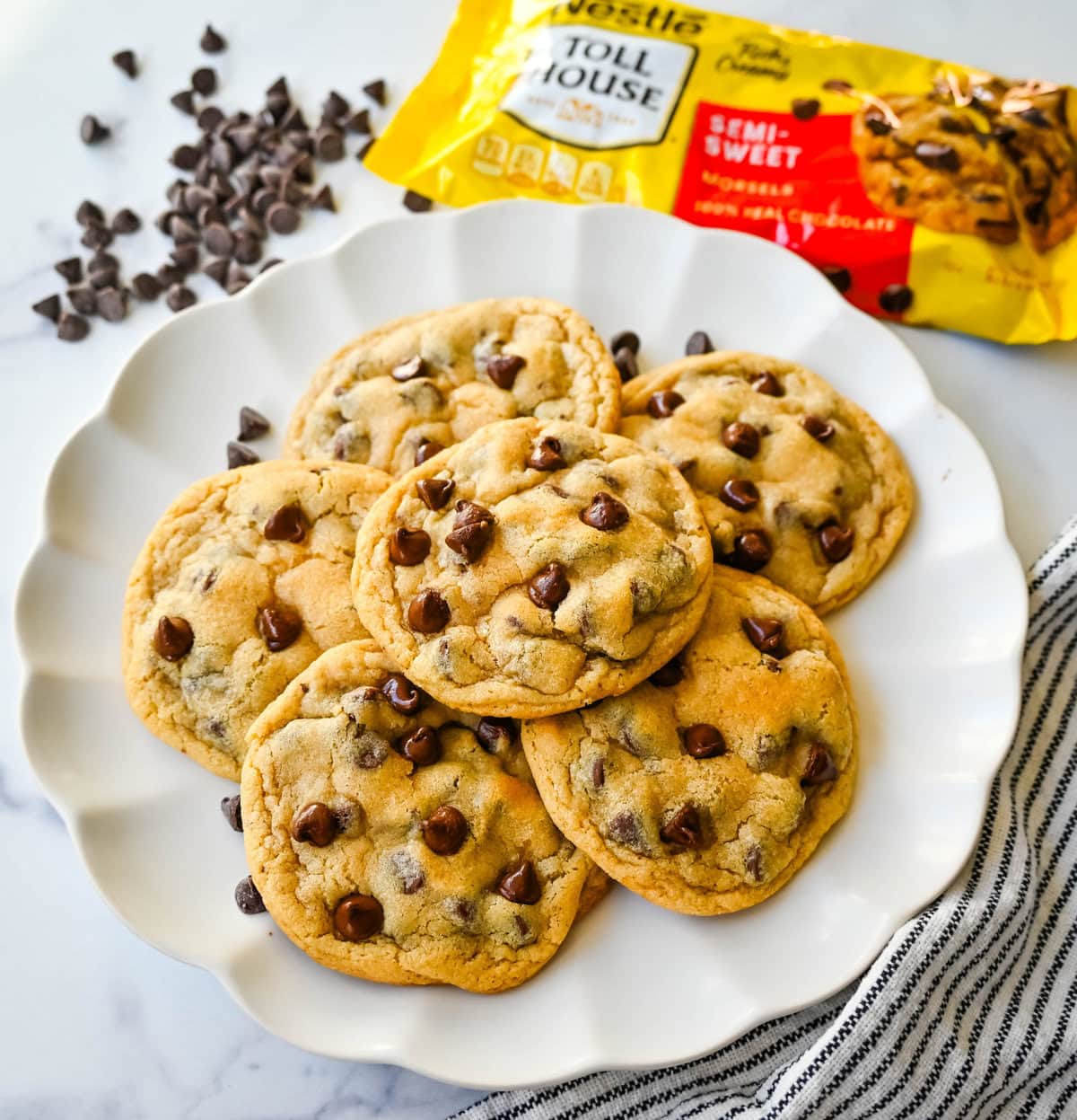 The Nestle Toll House Chocolate Chip Cookie Recipe. How to make the original Toll House chocolate chip cookie recipe on the bag. Tips for making the best Toll house chocolate chip cookies. Chocolate chip cookies on a plate with a yellow Nestle Toll House chocolate chips bag. Homemade chocolate chip cookies stacked on a plate made with Nestle toll house chocolate chips.