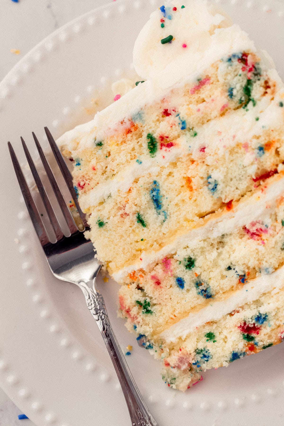 A piece of funfetti or confetti cake with sprinkles. A fluffy homemade Funfetti birthday cake with rainbow sprinkles topped with a light cream cheese buttercream frosting and an array of sprinkles. This Confetti Cake recipe is the perfect birthday cake!