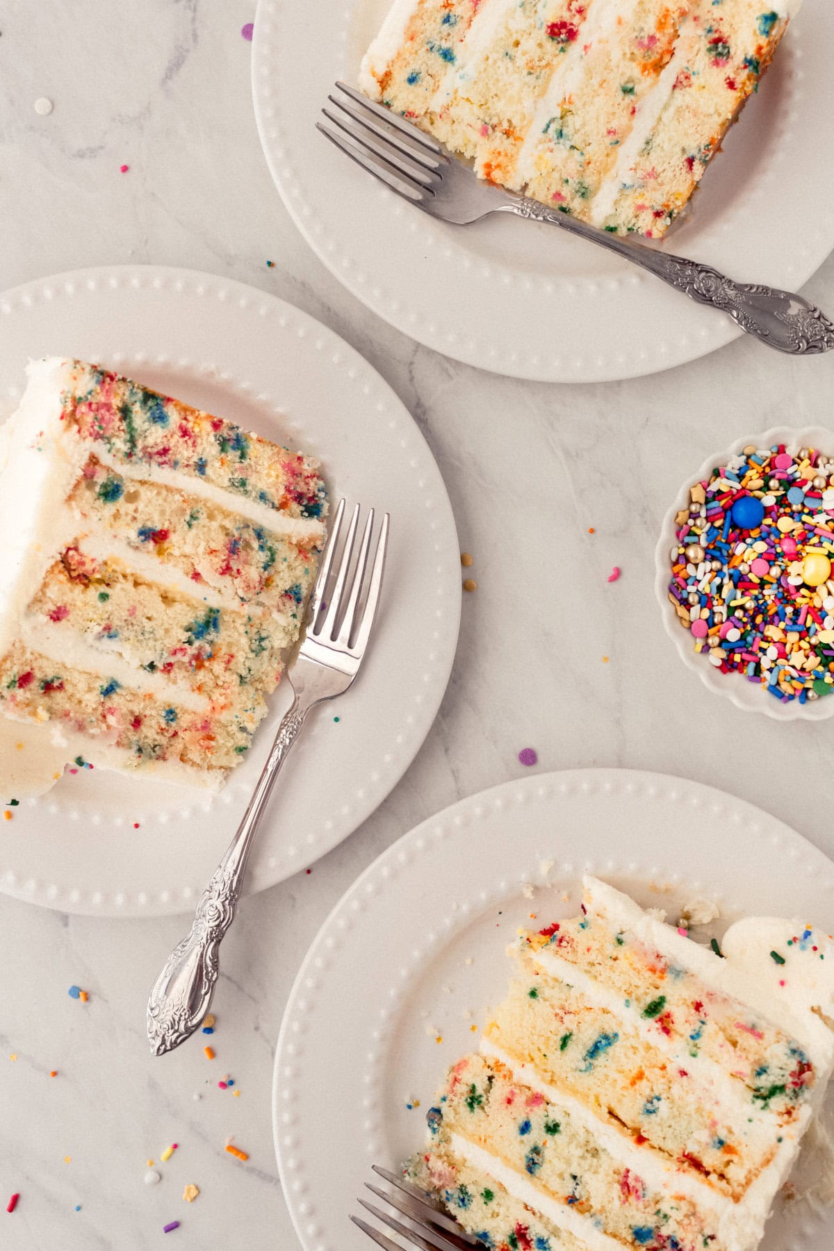 Cut pieces of birthday sprinkle cake. A fluffy homemade Funfetti birthday cake with rainbow sprinkles topped with a light cream cheese buttercream frosting and an array of sprinkles. This Confetti Cake recipe is the perfect birthday cake!