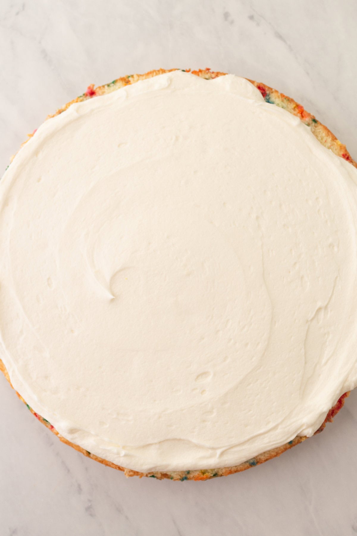 Frosting a homemade funfetti cake or confetti cake with vanilla frosting