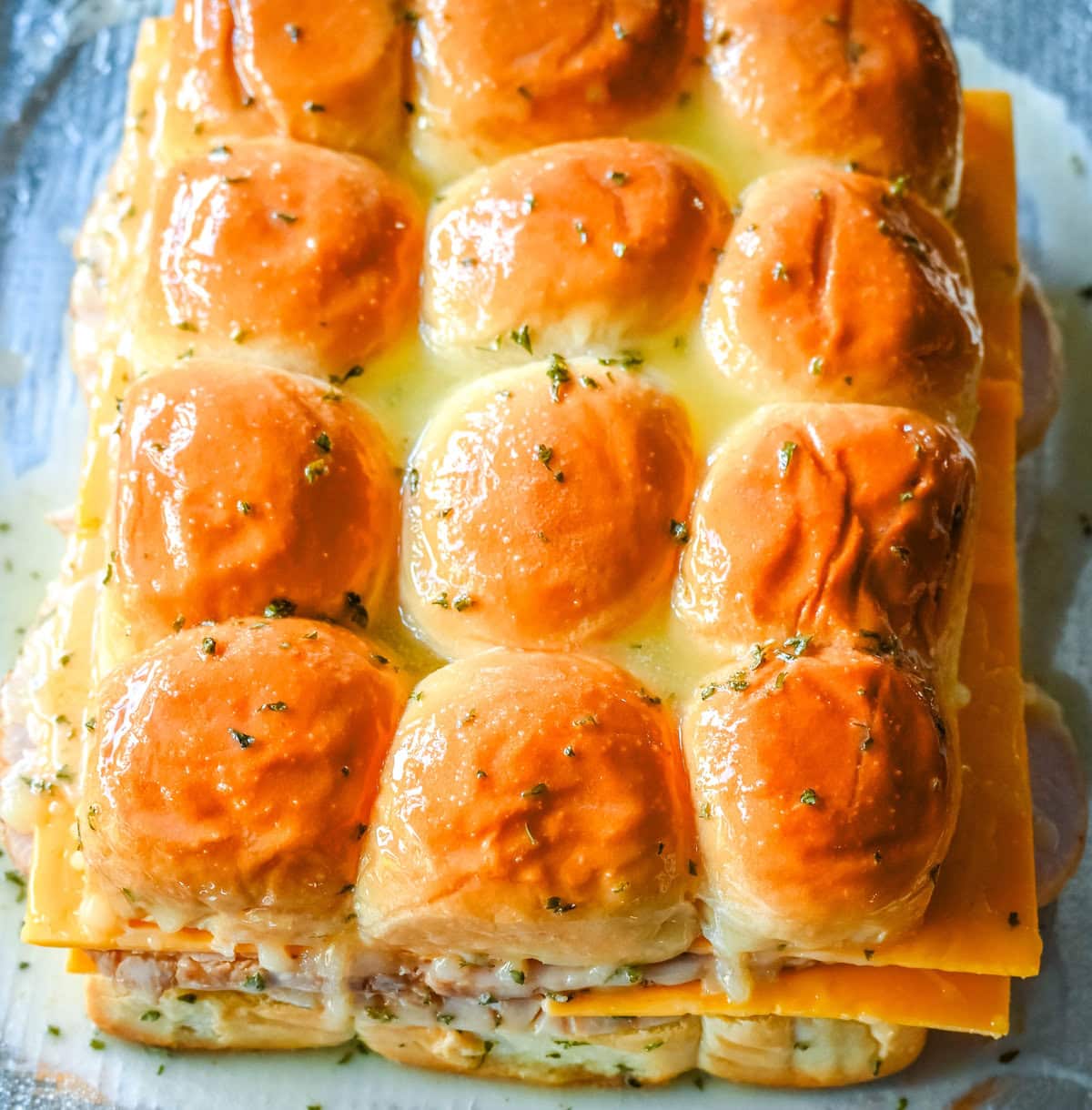 Brushing garlic butter over turkey cheddar sliders on hawaiian rolls