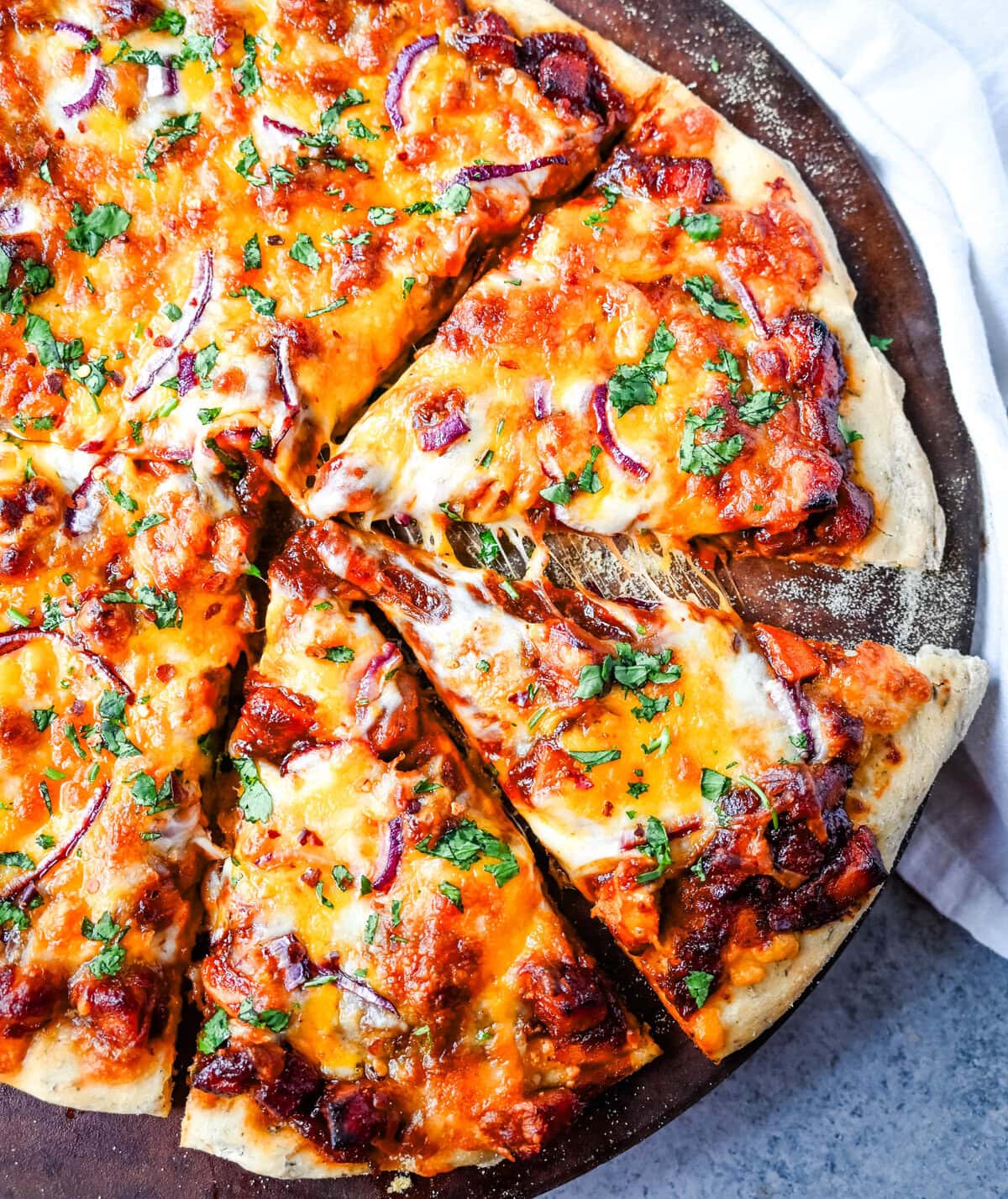 This Homemade BBQ Chicken Pizza is made with a Homemade Pizza Crust, BBQ Ranch Sauce, Mozzarella and Cheddar Cheeses, Red Onion, and a touch of Cilantro.  THE BEST BBQ CHICKEN PIZZA RECIPE.