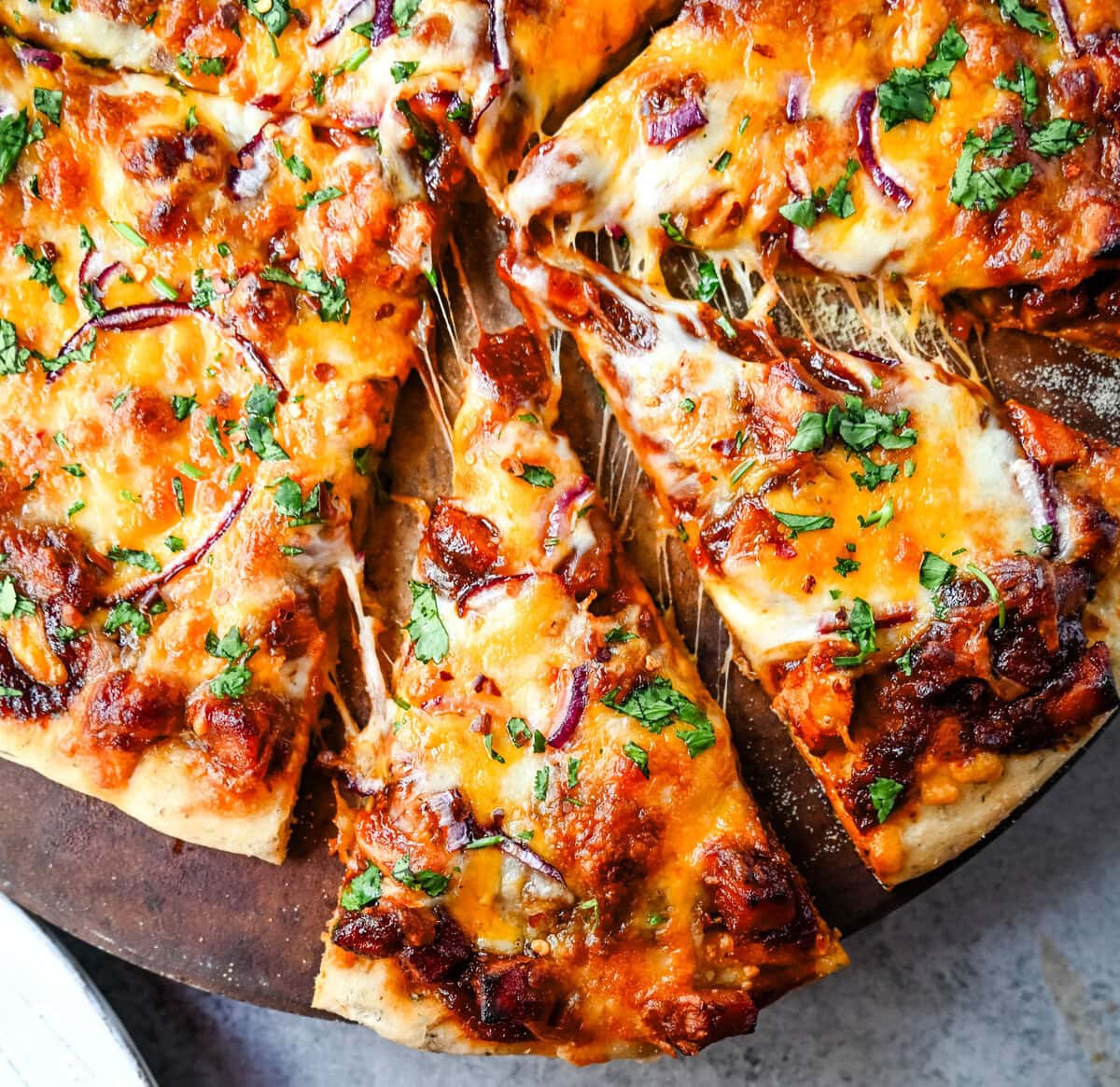 This Homemade BBQ Chicken Pizza is made with a Homemade Pizza Crust, BBQ Ranch Sauce, Mozzarella and Cheddar Cheeses, Red Onion, and a touch of Cilantro.  THE BEST BBQ CHICKEN PIZZA RECIPE.