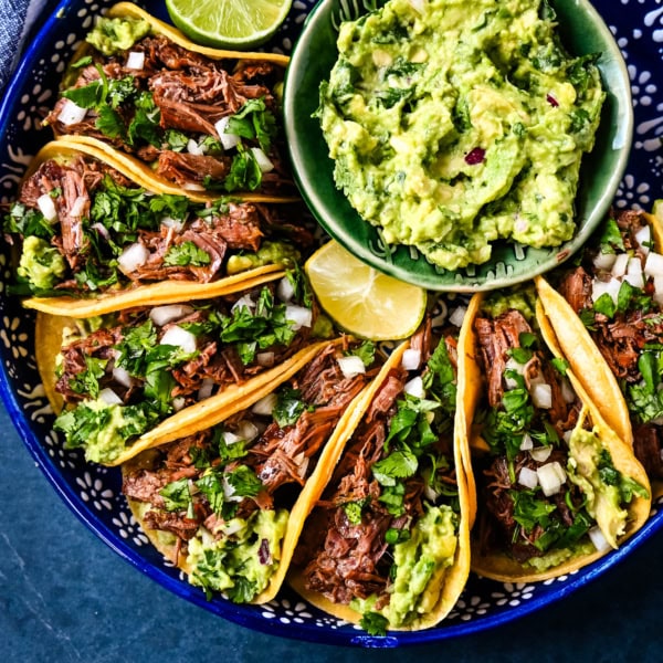 Tender, juicy, flavorful shredded beef with corn tortillas, fresh homemade guacamole, and a touch of cilantro and onion. These Slow Cooker Beef Tacos are so easy to make and everyone loves them!