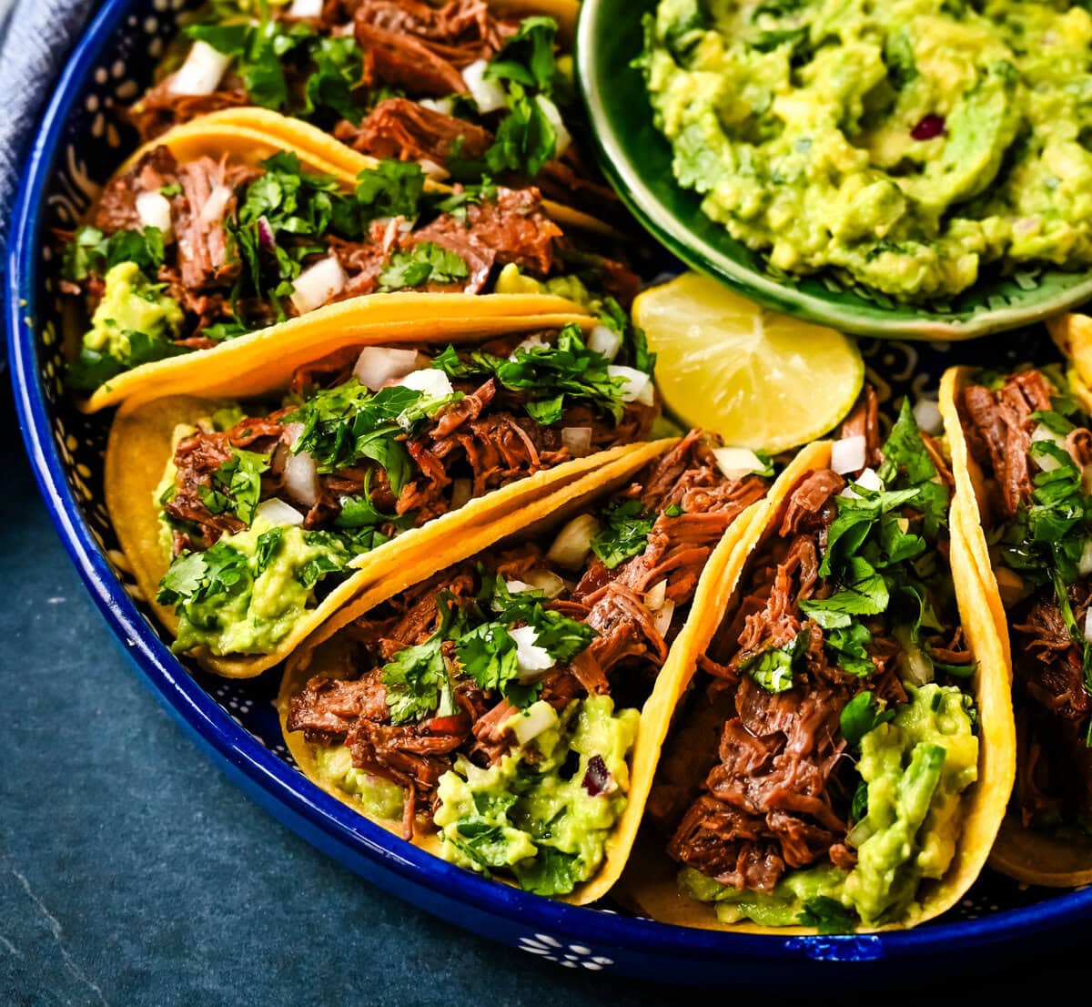 Tender, juicy, flavorful shredded beef with corn tortillas, fresh homemade guacamole, and a touch of cilantro and onion. These Slow Cooker Beef Tacos are so easy to make and everyone loves them!