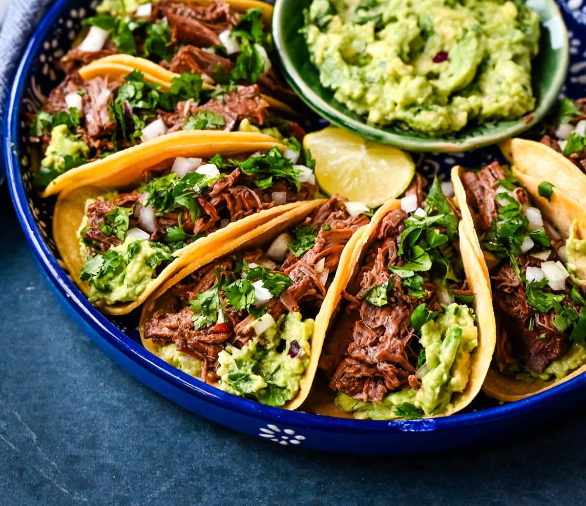 Tender, juicy, flavorful shredded beef with corn tortillas, fresh homemade guacamole, and a touch of cilantro and onion. These Slow Cooker Beef Tacos are so easy to make and everyone loves them!