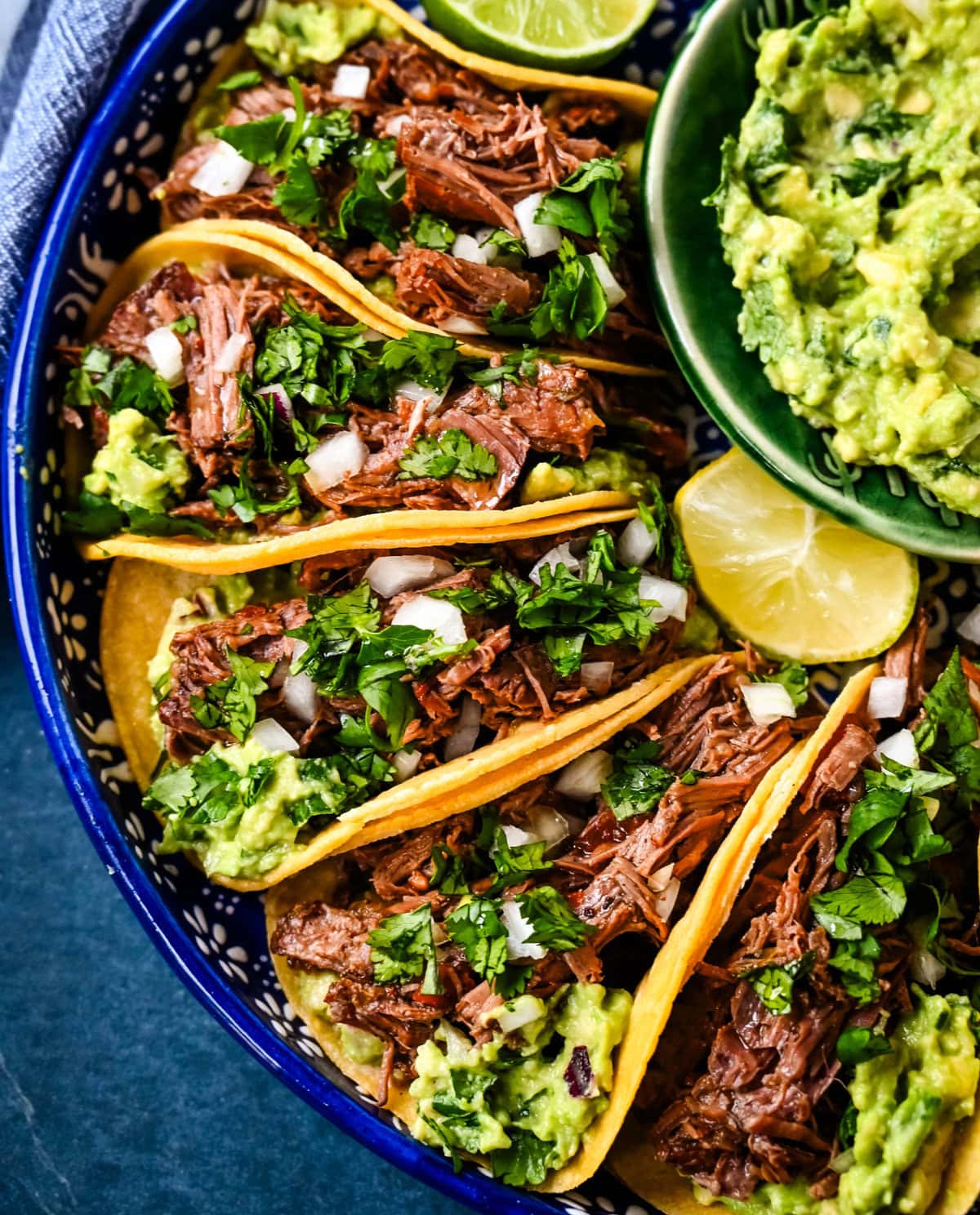 Tender, juicy, flavorful shredded beef with corn tortillas, fresh homemade guacamole, and a touch of cilantro and onion. These Slow Cooker Beef Tacos are so easy to make and everyone loves them!