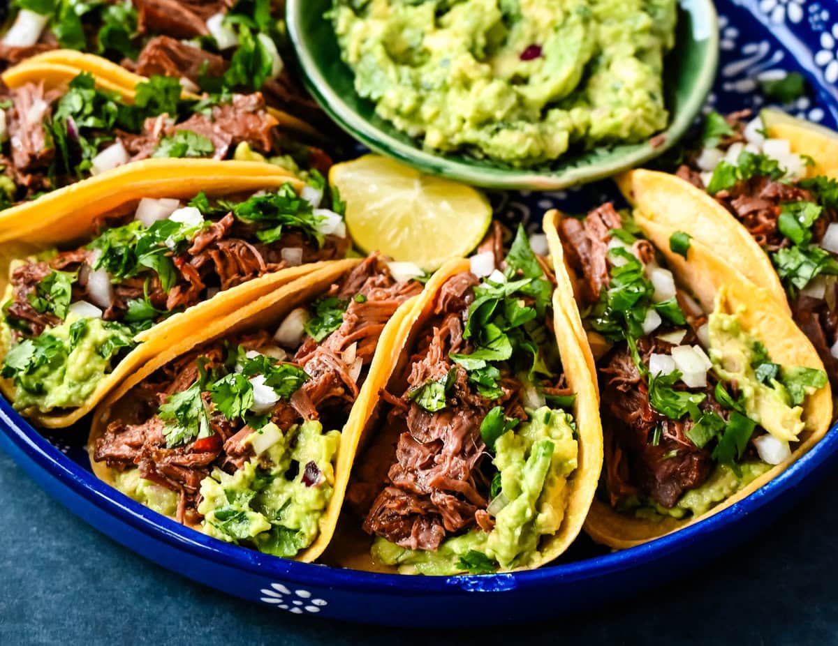 Tender, juicy, flavorful shredded beef with corn tortillas, fresh homemade guacamole, and a touch of cilantro and onion. These Slow Cooker Beef Tacos are so easy to make and everyone loves them!