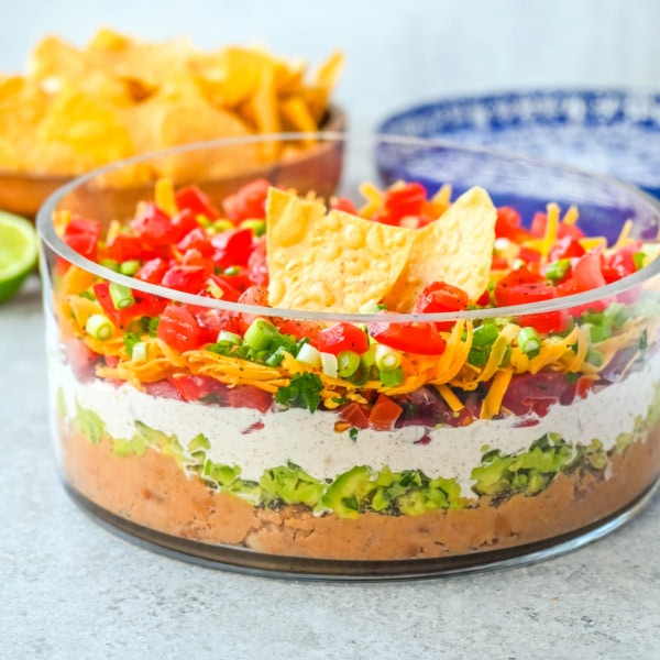 Seven-layer dip is a colorful, Tex-Mex-inspired appetizer featuring layers of refried beans, guacamole, seasoned sour cream, salsa, shredded cheese, fresh tomatoes, and sliced black olives. It’s popular because it’s easy to make, makes a stunning presentation, is delicious, and always a hit at parties or game-day gatherings. Whether you’re hosting a Super Bowl watch party or a casual family get-together, a classic 7 layer dip is guaranteed to impress.