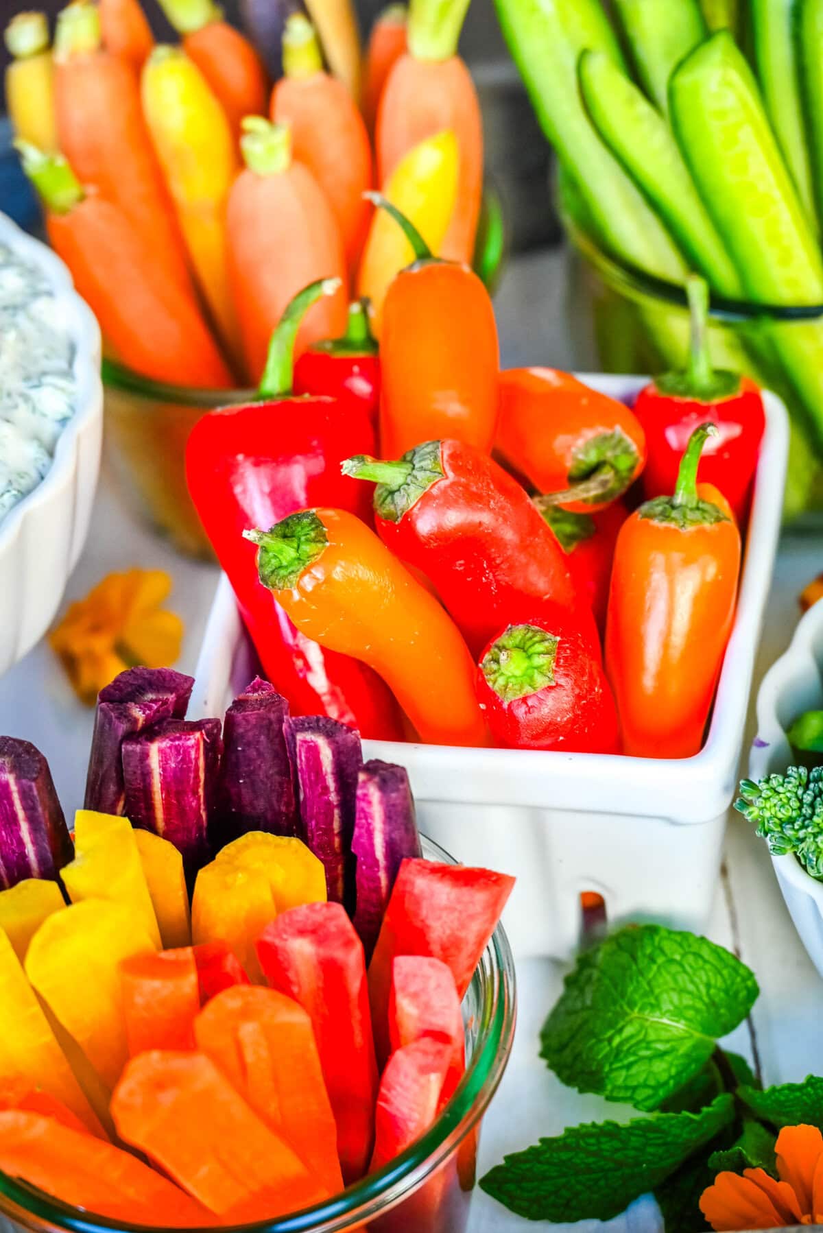 Mini sweet peppers, heirloom rainbow carrots, heirloom orange carrots, and cucumbers on a crudite platter or vegetable board.